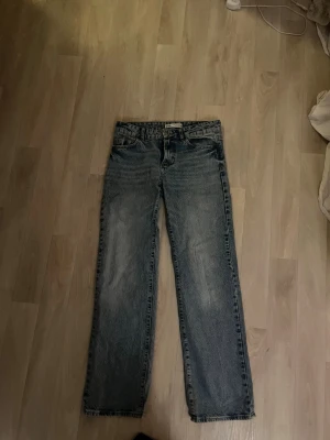 Blå raka jeans från Zara - Säljer ett par klassiska blå jeans från Zara i rak modell. Jeansen har en snygg tvättad look, fem fickor och normal midja. Tillverkade i tåligt denim med dragkedja och knapp framtill. Perfekta till sneakers eller boots.