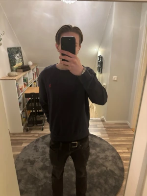 Mörkblå sweatshirt från Polo - Säljer en mörkblå sweatshirt från Polo med klassisk röd broderad logga på bröstet. Tröjan har rund halsringning och långa ärmar, perfekt för en clean och stilren look. Passar dig som gillar enkel men snygg streetstil.