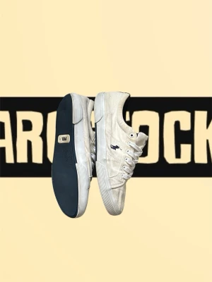 Vita sneakers från Polo Ralph Lauren - Säljer ett par vita sneakers från Polo Ralph Lauren med klassisk låg profil och marinblå logga på sidan. Skorna har vit textilovandel, vita snören och en robust gummisula med mörkblå undersida. Perfekta för en clean och stilren look.