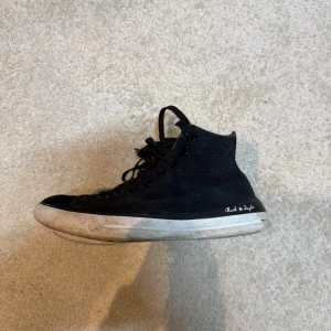 Svarta Converse Chuck Taylor sneakers - Säljer ett par klassiska svarta Converse Chuck Taylor high tops med svart snörning och vit sula. Skorna har rund tå och är tillverkade i mocka material med diskret logga på sidan. Perfekta för dig som gillar en tidlös streetstil.