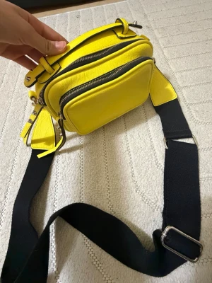 Gul axelväska från Don Donna - Säljer en riktigt snygg gul axelväska från Don Donna. Väskan har flera fack med dragkedja, bred svart axelrem och är gjord i ett mjukt skinnliknande material. Perfekt för dig som vill sticka ut med en färgklick i din outfit!😜💕 