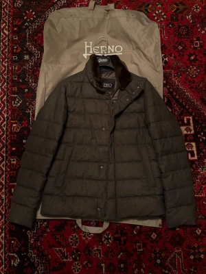 Herno jacka med pälskrage  - Säljer en grå pufferjacka från Herno med quiltad design och mjuk brun bäverpäls på kragen. Jackan har dragkedja och knappar framtill samt två sidofickor. Jackan är gjord i 100% ull. Nypris ligger mellan 13000-20000kr. Den är använd enstaka gånger och är fortfarande som ny. Storlek 50 sitter som en hyfsad M kan eventuellt även passa L. 