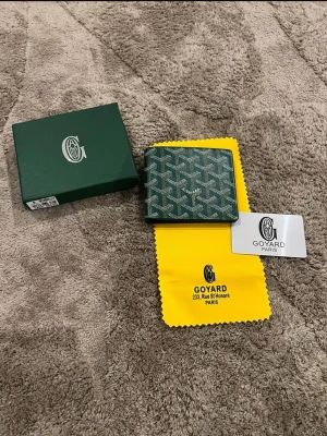  plånbok med mönster - Säljer en grön plånbok med ikoniska grafiska mönster. Plånboken har flera kortfack och är tillverkad i skinn med detaljer i vitt och grått. Kommer med original ask, tygpåse och kort. Perfekt för dig som vill ha något stilrent och lyxigt.