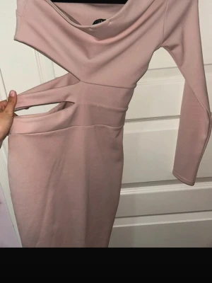 Ljusrosa cut out klänning - Trendig ljusrosa klänning med långa ärmar och coola cut out-detaljer i midjan. Klänningen har en kroppsnära passform och dragkedja i sidan (dragkedjan funkar ej, men är ihop sydd och syns inte när man har på sig den) för enkel påklädning. Perfekt för dig som vill sticka ut med en modern och edgy look.