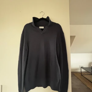 Mörkblå stickad tröja med krage - Säljer en mörkblå stickad tröja från These Glory Days. Tröjan har en uppvikt krage med v-ringad öppning och långa ärmar. Perfekt för dig som gillar en stilren och enkel look med lite extra edge. Tröjan är i ett jättebra skick (aldirg använd)