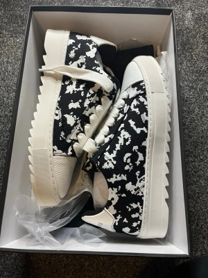 Svartvita sneakers från numeris  - Säljer ett par snygga svartvita sneakers från numeris  med coolt abstrakt mönster. Skorna har kraftig vit sula med taggig kant, snörning och detaljer i vitt skinn. Perfekta för dig som vill sticka ut med din stil. Väldigt unika storlek 42.