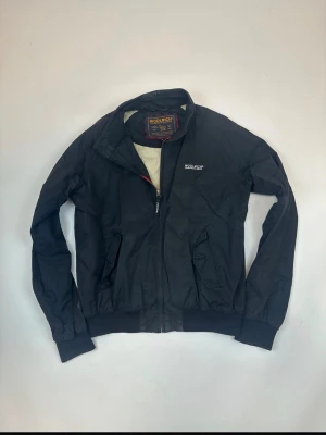 Svart vindjacka från Woolrich - Säljer en svart vindjacka från Woolrich med dragkedja framtill och två snedställda fickor. I väldigt bra skick den ända defekten är att en knop sitter löst och en har lossnat, men annars en jätte fin jacka för ett bra pris. Storlek M men sitter som S. Kom dm vid frågor😇
