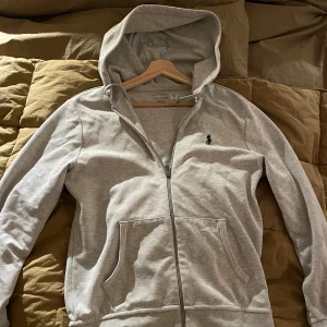 Grå ralph lauren zip luvtröja - Tröjan är i mycket bra skick. Jag säljer den för  jag växt ur den och inte längre kan använda den. Hör av dig om du har några frågor.