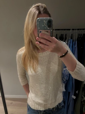 Glittrig stickad tröja från Vero Moda - Superfin ljus stickad tröja från Vero Moda med glittriga paljettdetaljer. Tröjan har rund halsringning, trekvartsärm och ribbade muddar. Perfekt att styla med jeans för en snygg look.