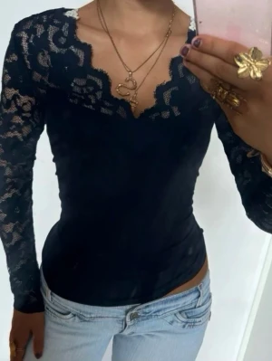 Svart spetsblus med v-ringning - Säljer en svart långärmad blus med transparenta spetsärmar och v-ringad kant med vågig spetsdetalj. Toppen har en elegant, feminin look. Perfekt för fest🩷