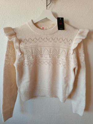 Vit stickad tröja med volang från Levi's helt ny med tagg - Levi’s Shane Flutter Sleeve Sweater Cut Stickad tröja, ny med tagg – aldrig använd. XS (passar även S/M). Axelbredd 38 cm, längd 53 cm.  Färg: Tofu. Ord. pris 899 kr – mitt pris 389 kr.