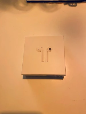 Apple AirPods 2 - Säljer ett par Apple AirPods 2 i fint skick med originalförpackning, laddningsetui och laddkabel. Hörlurarna är trådlösa och fungerar utmärkt. Laddningsetuiet har mindre ytslitage men inget som påverkar funktionen.