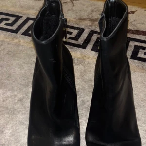 Svarta boots med klack och fyrkantig tå - Säljer ett par svarta boots i skinn med fyrkantig tå och rejäl klack. Snygg minimalistisk design med dragkedja på sidan för enkel på- och avtagning. Perfekta för dig som gillar stilrena och trendiga skor med lite edge.