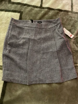 Grå rutig kortkjol från Lindex - Snygg grå kortkjol från Lindex med diskret rutigt mönster. Kjolen har en klassisk rak form, sidofickor och dold dragkedja i sidan. Materialet känns mjukt och har en lätt struktur, perfekt för att skapa en stilren look. Säljer pga att den inte passade mig aldrig använd