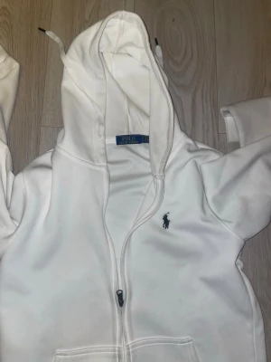 White Polo Ralph Lauren Zip Hoodie – Clean & Timeless Style  - Selling a white Polo Ralph Lauren zip-up hoodie, perfect for a clean, classic everyday look. Features a full front zipper, hood with drawstrings, and the iconic embroidered Polo logo on the chest. A versatile piece that works great for both casual and smart-casual outfits.  🧵 Details: 	•	Brand: Polo Ralph Lauren 	•	Color: White 	•	Style: Zip-up hoodie with hood 	•	Embroidered logo on chest 	•	Soft and comfortable fabric  📦 Condition: like new (see photos) 🚭 From a smoke- and pet-free