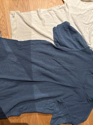 Två basic t-shirts i blått och beige - Säljer två enkla t-shirts, en i mörkblå och en i ljusbeige. Båda har klassisk rund hals och korta ärmar. Perfekta till jeans eller shorts för en clean och avslappnad stil. Materialet känns mjukt och skönt mot huden. Gjort av linne