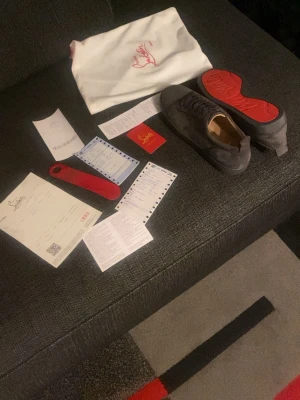 Grå mocka sneakers från Louboutin - Säljer ett par gråa sneakers från Christian Louboutin i mocka med klassisk röd sula och rund tå. Skorna har snörning och diskret logga på innersulan. Kommer med originalpåse och tillbehör. Perfekta för dig som vill ha något exklusivt och stilrent.