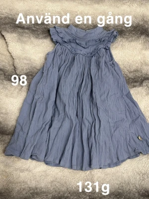 Blå klänning med volang - Supersöt blå klänning i mjukt och luftigt tyg. Klänningen har volangdetaljer vid axlar och halsringning samt är ärmlös. Perfekt för varma dagar och har en flowy passform som ger en skön känsla.🌸 Använd en gång. Storlek 98 