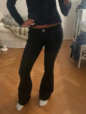 Svarta bootcut jeans med detaljer - Säljer ett par svarta bootcut jeans med låg midja och snygga silvriga nitar på bakfickorna. Jeansen har klassisk femficksdesign och är i stretchigt jeansmaterial. Perfekta om du gillar en lite retro vibe och vill ha något som sticker ut lite extra.