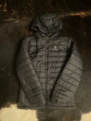 Svart pufferjacka från U.S. Polo Assn. - Svart pufferjacka med huva från U.S. Polo Assn. Jackan har quiltad design, dragkedja framtill och långärmade ärmar. Märkets logga syns på bröstet. Perfekt för kalla dagar och har en clean, sportig look. Storlek 12/13y och är aldrig använd. Kontakta vid fråga👍