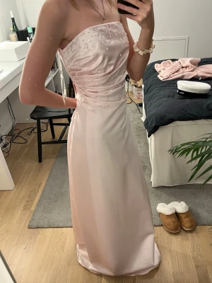 Ljusrosa axelbandslös balklänning - JAG HAR STORLEK XS/XXS OCH KLÄNNINGEN ÄR STORLEK S! Supersnygg ljusrosa långklänning i satin med axelbandslös design. Perfekt till student, bröllop eller bal! Klänningen har en elegant och figurnära passform. Passar inte mig som man kan se, därför håller jag den så man kan se ungefär hur den ser ut på någon med storlek S. 🩷🩷