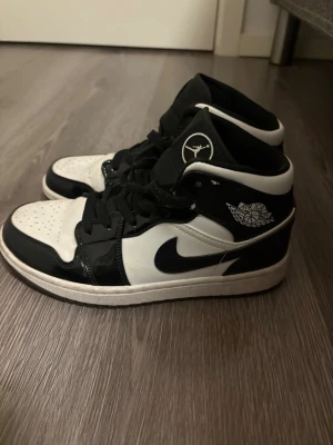 Nike Air Jordan 1 svart/vit EUR 38 - Säljer ett par Nike Air Jordan 1 i svart och vitt. Klassisk high-top siluett med svart swoosh, vita paneler och svarta detaljer. Skorna har snörning, rund tå och perforerad tåbox. Tillverkade i skinn och syntetmaterial. Ikonisk Jumpman-logga på plösen och Air Jordan-märke på sidan.