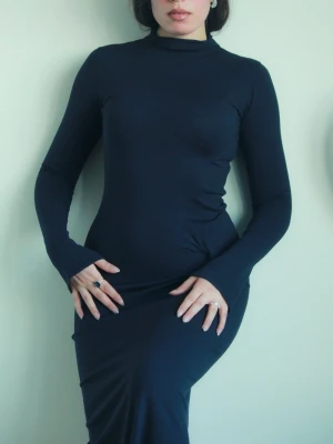 Mörkblå långärmad långklänning - Säljer en stilren mörkblå långklänning med polokrage och lång ärm. Klänningen har en tight passform och är gjord i ett mjukt, stretchigt material som sitter snyggt på kroppen. Perfekt för dig som gillar minimalistisk och elegant stil. Det finns ett litet hål i klänningen