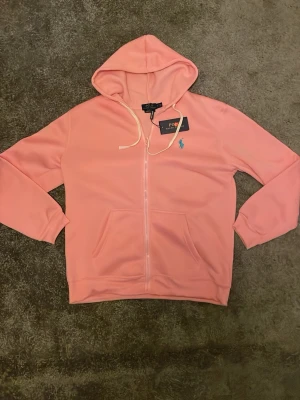 Polo Ralph Lauren zip - En helt ny polo zip i färgern rosa. Den rosa färger är mycket fin och logan är ljusblå som passar in bra till det rosa. Kom med deals!
