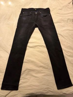 Lee svarta slim jeans W30 L32 - Säljer ett par svarta Lee slim jeans i storlek W30 L32. Jeansen har klassisk femficksdesign, smal passform och är tillverkade i stretchig bomullsdenim för extra komfort. Perfekta till sneakers eller boots.