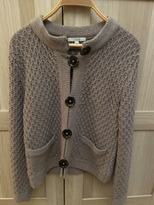 Gammalrosa stickad kofta från Dagmar - Säljer en  stickad kofta från Dagmar i storlek S. Färgen är dov gammelrosa med inslag av viollila. Koftan har ett snyggt strukturmönster, stora knappar framtill och två fickor. Perfekt till lager på lager under höst och vinter. Klassisk och enkel att matcha med det mesta.