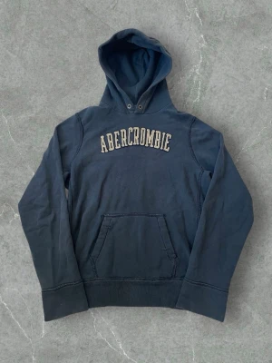 Abercrombie & Fitch Navy Blue Hoodie – Size XL - Abercrombie hoodie in blue with “Abercrombie” text on the front. Features a slightly distressed, worn-in design that gives a vintage look. Soft and comfortable. Size XL.