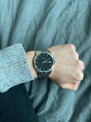 Svart Calvin Klein klocka i stål - Calvin Klein klocka med svart urtavla och datumvisning | Armbandet är i blankt rostfritt stål och har en klassisk länkdesign | Skick 9/10 | använd under en månad | Tveka inte att höra av vid frågor! Nypris 2500