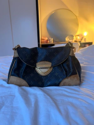 Louis Vuitton monogram axelväska - Säljer en klassisk Louis Vuitton axelväska i mörkbrunt monogrammönster med beigea skinn-detaljer och guldfärgat spänne. Väskan har justerbar axelrem och ikoniska LV-loggor över hela ytan. Jag köpte den på Vinted för ett tag sedan men har inte användning för den. Jag skickade den till varifieringcenter för att kolla så att den var äkta. Beviset finns bland bilderna på väskan. Väskan har några defekter men ni får gärna höra av er om ni vill se fler bilder eller om ni har några frågor☺️💕