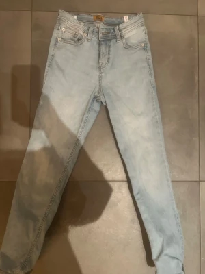 Ljusblå jeans från Jack & Jones, 146 - Säljer ett par ljusblå jeans från Jack & Jones i storlek 146 (11 år). Klassisk femficksmodell med raka ben och normal passform. Jeansen har snygga slitningar och är tillverkade i mjukt denimtyg för skön känsla. Perfekta till vardagslooken!