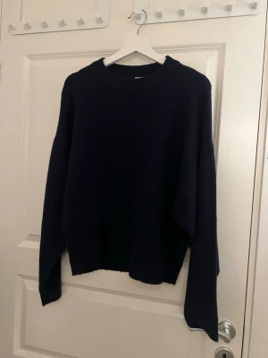 Mörkblå stickad tröja från Nelly - Mysig mörkblå stickad tröja från Nelly i storlek S. Tröjan har en enkel, rak passform med ribbad rund halsringning och långa ärmar. Perfekt för kyliga dagar och enkel att styla till olika outfits.