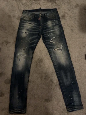 Dsquared2 jeans  - Säljer ett par mörkblå skinny jeans med slitna detaljer, färgstänk och hål på benen. Jeansen har en tvättad look och smal passform som sitter tajt längs benen. Perfekta för dig som gillar en edgy och trendig stil. Pris kan diskuteras, tar även emot byten