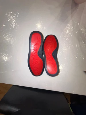 Mörkblå sneakers från Christian Louboutin - Säljer ett par mörkblå sneakers från Christian Louboutin med klassisk röd sula och snygg snörning. Skorna är i mocka och har en rund tå samt platt sula. Perfekta för dig som vill sticka ut med exklusiva detaljer och ikonisk design. Köpta på plick. Skolåda och dustbag följer inte med. Priset är inte hugget i sten😁!