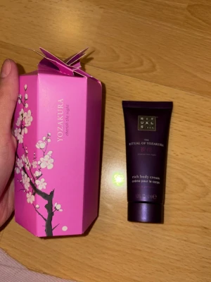 Rituals Yozakura body cream - Ritual of Yozakura rich body cream i en mörklila tub, 40 ml. Kommer i en snygg rosa presentförpackning med körsbärsblommor. Innehåller Yoshino cherry och svart ris, 95% naturligt ursprung. Ger näring och doftar intensivt.Helt oanvänd! 