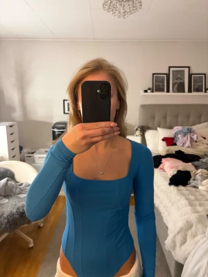 Blå långärmad bodysuit från H&M - Säljer en blå långärmad bodysuit från H&M med fyrkantig urringning och figurnära passform. Toppen är tillverkad i mjuk bomull och har sömmar som ger en snygg detalj. Aldrig använt. 