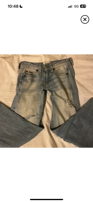Ljusblå baggy jeans från Urban outfitters  - Baggy ljusblå Jean från urban outfitters med slitna detaljer och hål på benen. Jeansen har låg midja , raka ben och klassisk femficksdesign. Materiallet är i bomull och fåtal gånger använda. W26. Passar som XS/S/34/36 