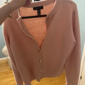 Ljusrosa kofta - Superfin ljusrosa kofta från New Look i mjukt stickat material. Klassisk rund halsringning, långa ärmar och snygga guldfärgade knappar framtill. Perfekt att slänga över en topp för en chill och söt look. Rätt så nopprig dock därav priset🩷