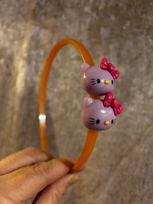 Hello Kitty diadem i olika färger - Färgglada diadem i plast med två Hello Kitty-huvuden på varje. Finns i lila, blått, gult och rosa, alla med kontrasterande rosetter. Perfekt accessoar för dig som vill sticka ut med en söt och lekfull look. 35kr/st 