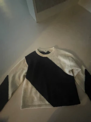 Svartvit stickad tröja med diagonal mönster - Säljer en stickad tröja i svart och vitt med ett snyggt diagonalt mönster över hela framsidan och ärmarna. Tröjan har rund hals och långa ärmar, perfekt för dig som gillar grafiska kontraster och vill ha en unik look.