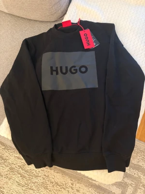 Hugo sweatshirt S - en helt ny HUGO-tröja i storlek S:  ✨ Helt ny HUGO-tröja – Storlek S ✨  Säljer en oanvänd, svart HUGO-tröja i storlek S. Den har en snygg, minimalistisk design med en grå HUGO-logga på bröstet. Perfekt för dig som vill ha en stilren och bekväm tröja av hög kvalitet.  *   Märke: HUGO *   Storlek: S *   Färg: Svart med grå logga *   Skick: Helt ny, aldrig använd *   Modell: Sweatshirt med rund hals  Passa på att fynda en exklusiv tröja som aldrig blivit använd! Perfekt som present eller för att up