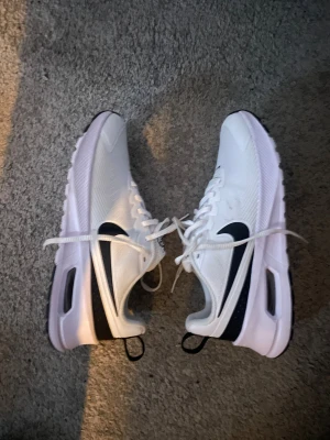 Nike Air Max vita sneakers - Nike Air Max sneakers i fräsch vit färg med svarta detaljer och klassisk swoosh på sidan. Skorna har en synlig Air Max-dämpning i sulan, snörning och rund tå. Ovandelen är i syntetmaterial med mesh för extra ventilation. Perfekt för dig som gillar sportig och clean stil.