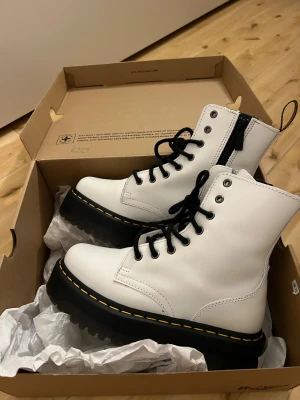 Vita Dr. Martens boots med platåsula - Säljer ett par vita Dr. Martens boots i skinn med kraftig platåsula och klassisk gul söm. Skorna har svarta snören, dragkedja på sidan och grovt mönstrad sula för extra grepp. Perfekt för dig som vill sticka ut med en edgy stil. De är nästan helt nya med boxen kvar, ändast använd en gång innan. 