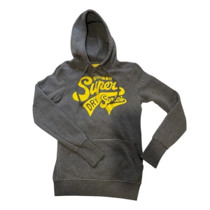 Grå hoodie från Superdry med tryck - Snygg grå hoodie från Superdry med stort gult tryck på bröstet. Tröjan är i storlek S men passar XS bättre. 