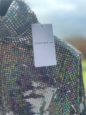 Glittrig polotopp från Dodo Bar Or - Säljer en maxad glittrig polotopp från Dodo Bar Or. Toppen har ett rutigt mönster i holografiska färger som skiftar i silver, blått, lila och grönt. Långärmad och figurnära modell med hög krage, perfekt för att sticka ut. Materialet är glittrigt och känns lyxigt.