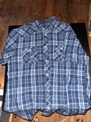 Blårutig slim fit skjorta KappAhl - Snygg blårutig skjorta från KappAhl i slim fit-modell. Skjortan har klassisk krage, två bröstfickor med knappar och vita knappar framtill. Tillverkad i mjuk bomull som känns skön mot huden. Perfekt för dig som gillar stilrena rutor och en smalare passform.