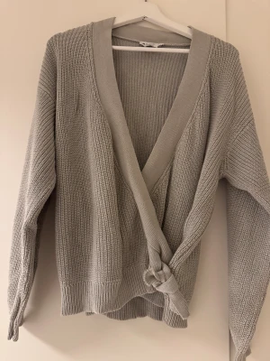 Grå omlottkofta från NA-KD - Snygg grå stickad omlottkofta från NA-KD med bred ribbad kant och knyt framtill. Koftan har långärmad design och djup v-ringning, perfekt för lager-på-lager. Mjuk och skön känsla i materialet, passar dig som gillar chill och stilren look.